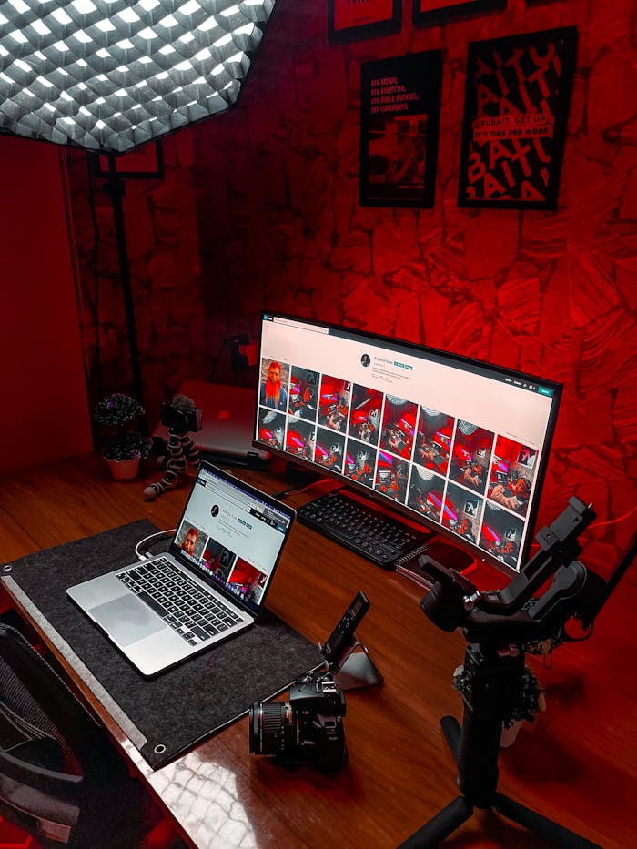 Stylish video editing setup featuring laptop and ultrawide monitor with striking red lighting.